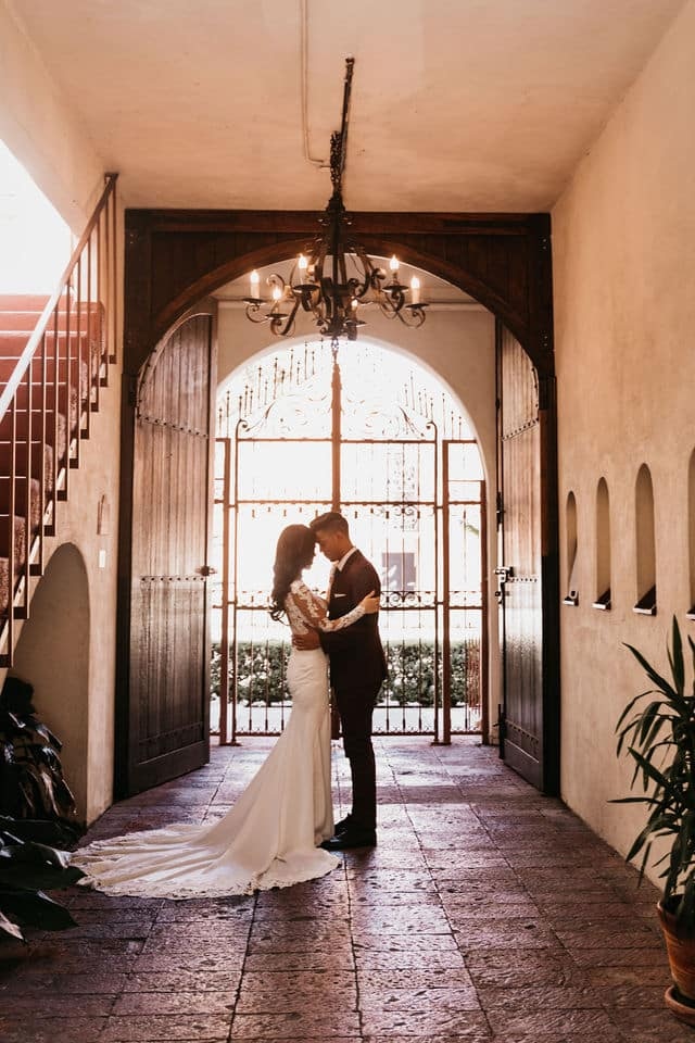 Couple forehead to forehead in a tiled archway beneath a wrought-iron chandelier