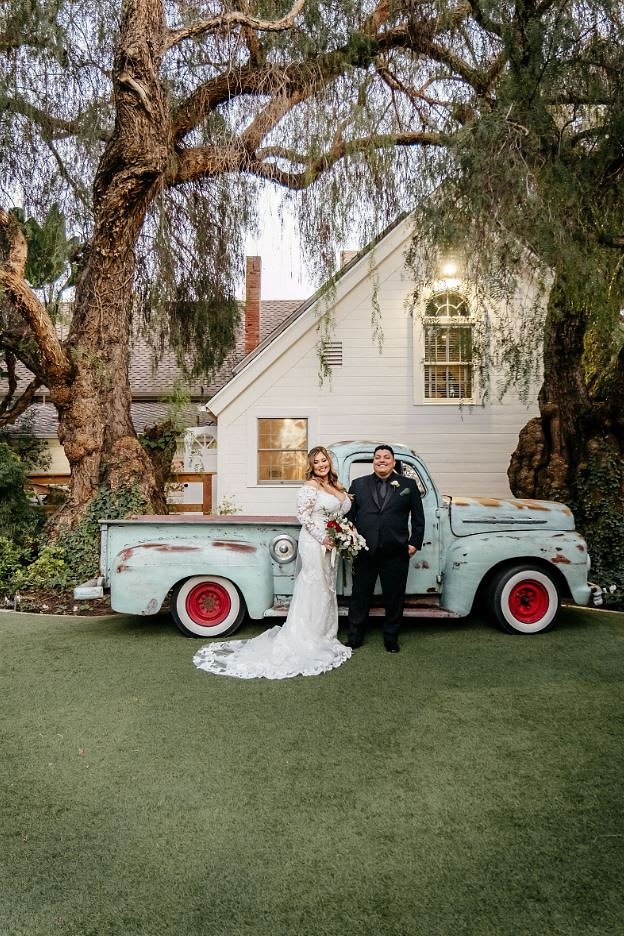 Bride and groom in front of a vintage turquoise pickup truck beneath a willow tree