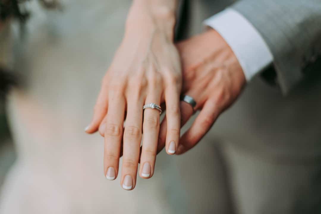 Close-up of a couple's hands overlapping after the ceremony, her engagement ring above his plain wedding band