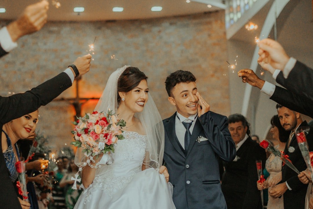 Newlyweds walking a sparkler-lined aisle, guests holding sparklers overhead as the groom wipes his eye