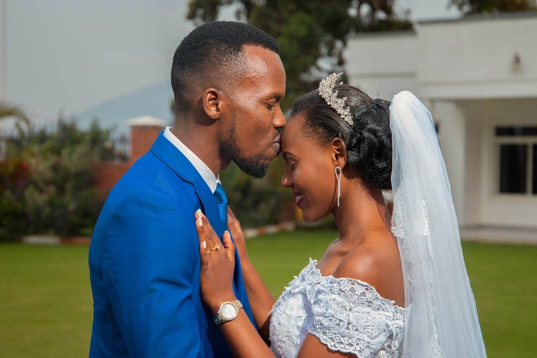 Groom in a bright blue suit kissing his bride's forehead, her hand resting on his chest and her veil trailing behind