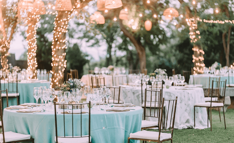 Garden reception laid with mint-green linen and glassware under woven lanterns and strings of fairy lights in the trees