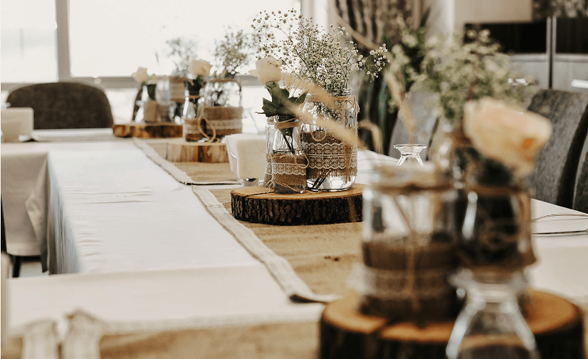Rustic reception table with burlap runners, wood-slice rounds and jars of baby's breath and roses