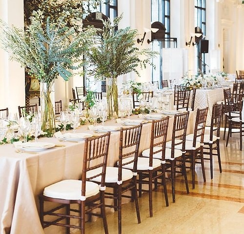 Long banquet table at the James Leary Flood Mansion, set with dark chiavari chairs and tall greenery centerpieces