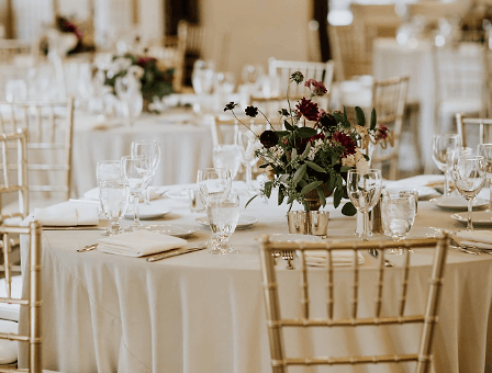 Round reception tables at Berkeley City Club laid with ivory linen, gold chiavari chairs and a burgundy flower centerpiece