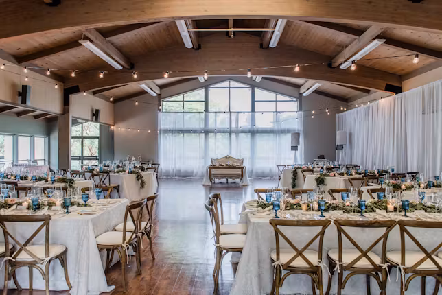 Reception hall at the Garden at Heather Farms, with a vaulted wooden ceiling, string lights and long tables of cross-back chairs