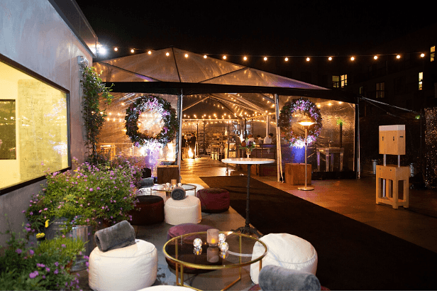 The rooftop terrace at The Pearl SF at night, with floral wreaths on a lit clear tent, string lights and low lounge seating