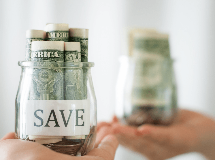 Hands holding glass jars of rolled dollar bills, the nearest labeled SAVE