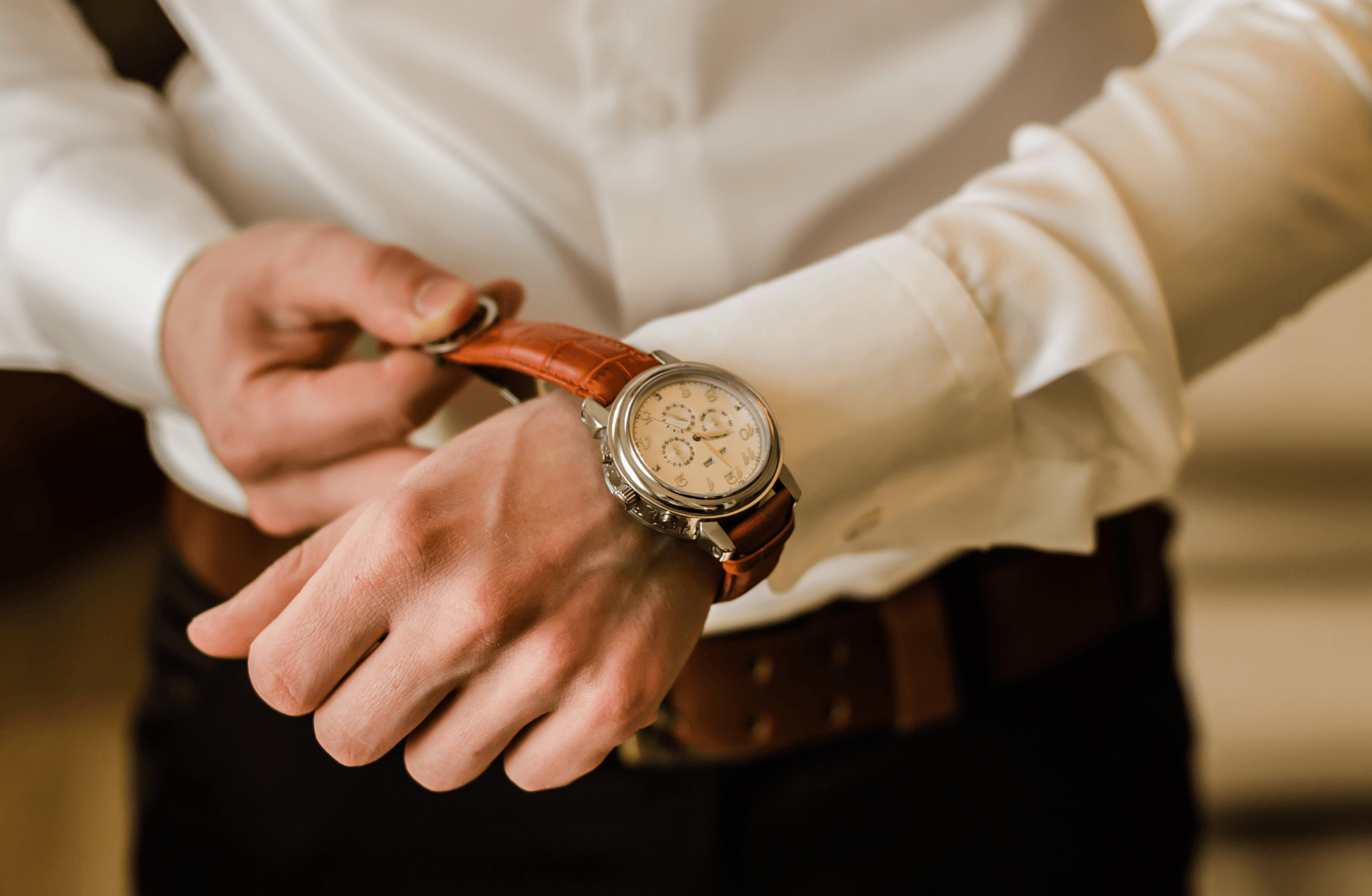 Groom fastening a leather-strap watch at the cuff of a white dress shirt