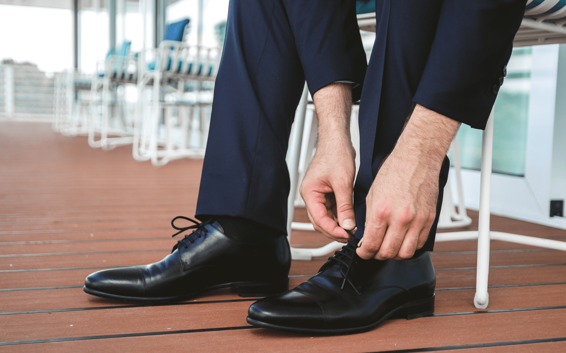 Groom in navy suit trousers lacing up black cap-toe oxford shoes