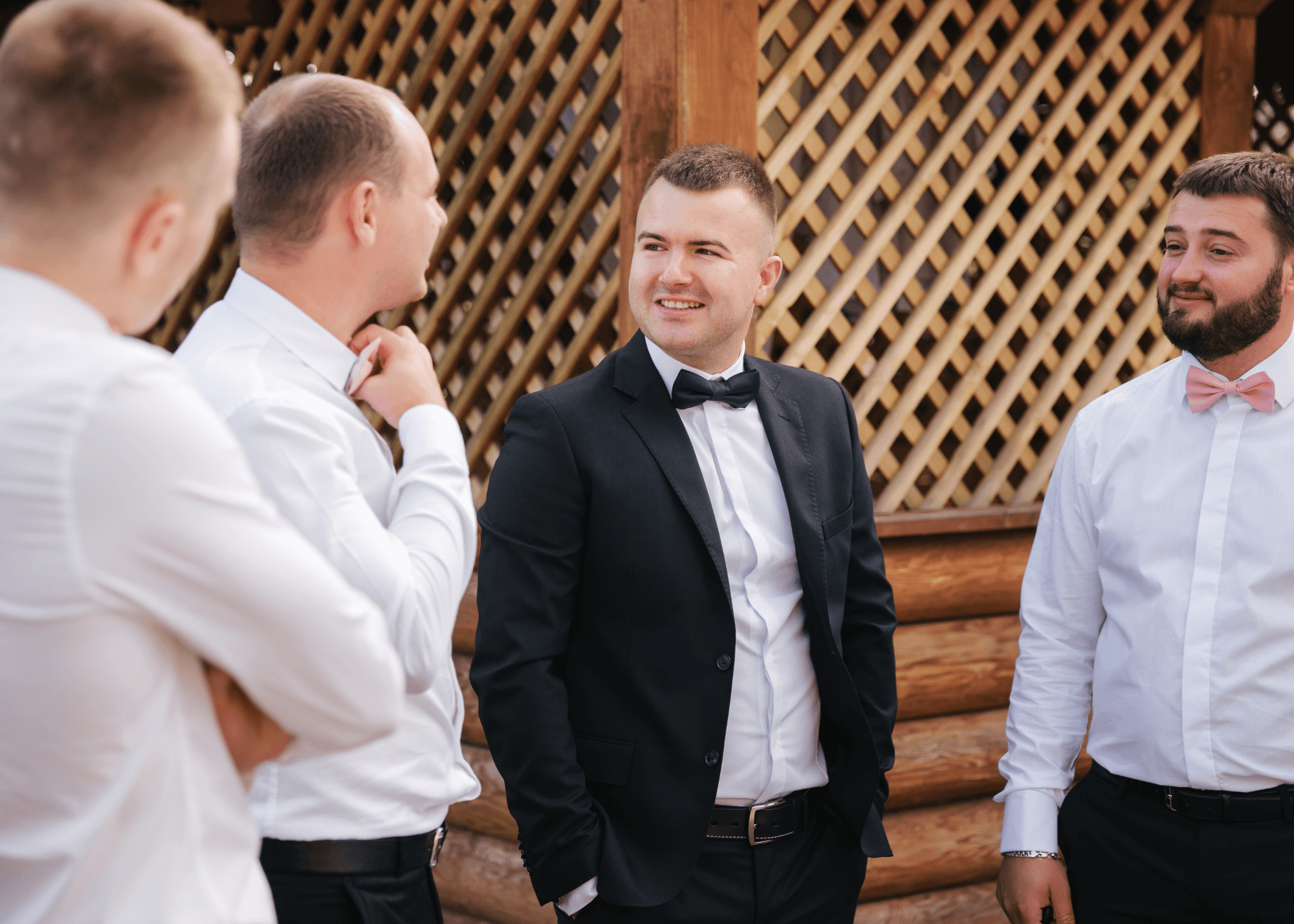 Groom in a black suit and bow tie laughing with groomsmen in white shirts and pink bow ties
