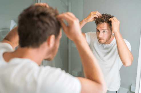 Groom styling tousled hair in a bathroom mirror