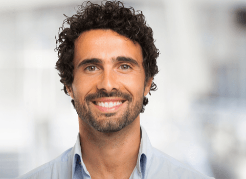 Man with curly dark hair and a trimmed beard, smiling broadly