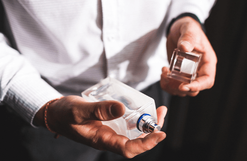 Man in a white shirt holding a bottle of cologne and its glass cap