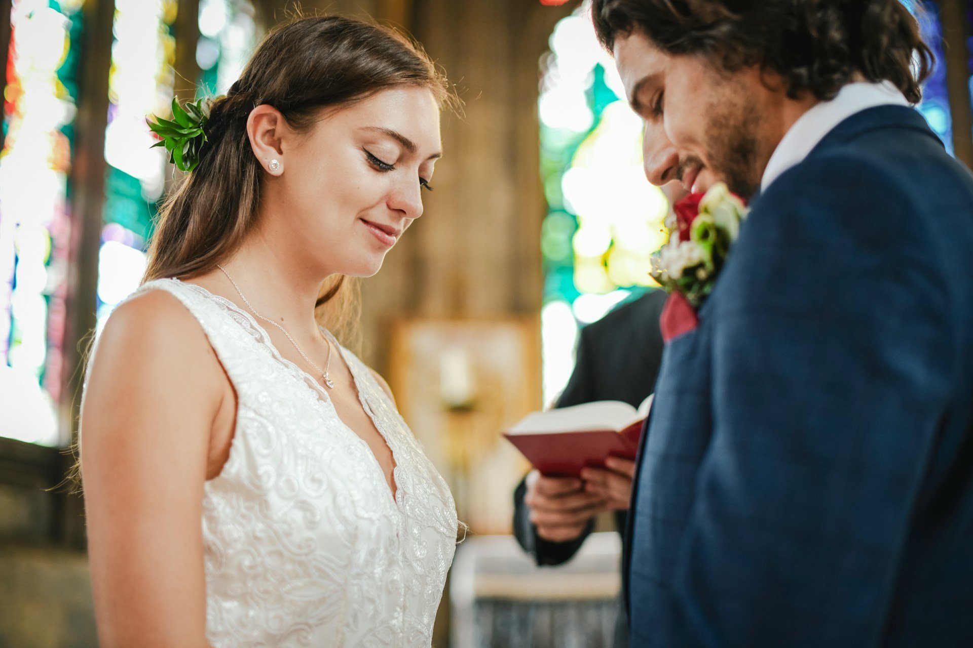 Bride and groom standing at the altar with heads bowed during the vows, stained glass glowing behind them