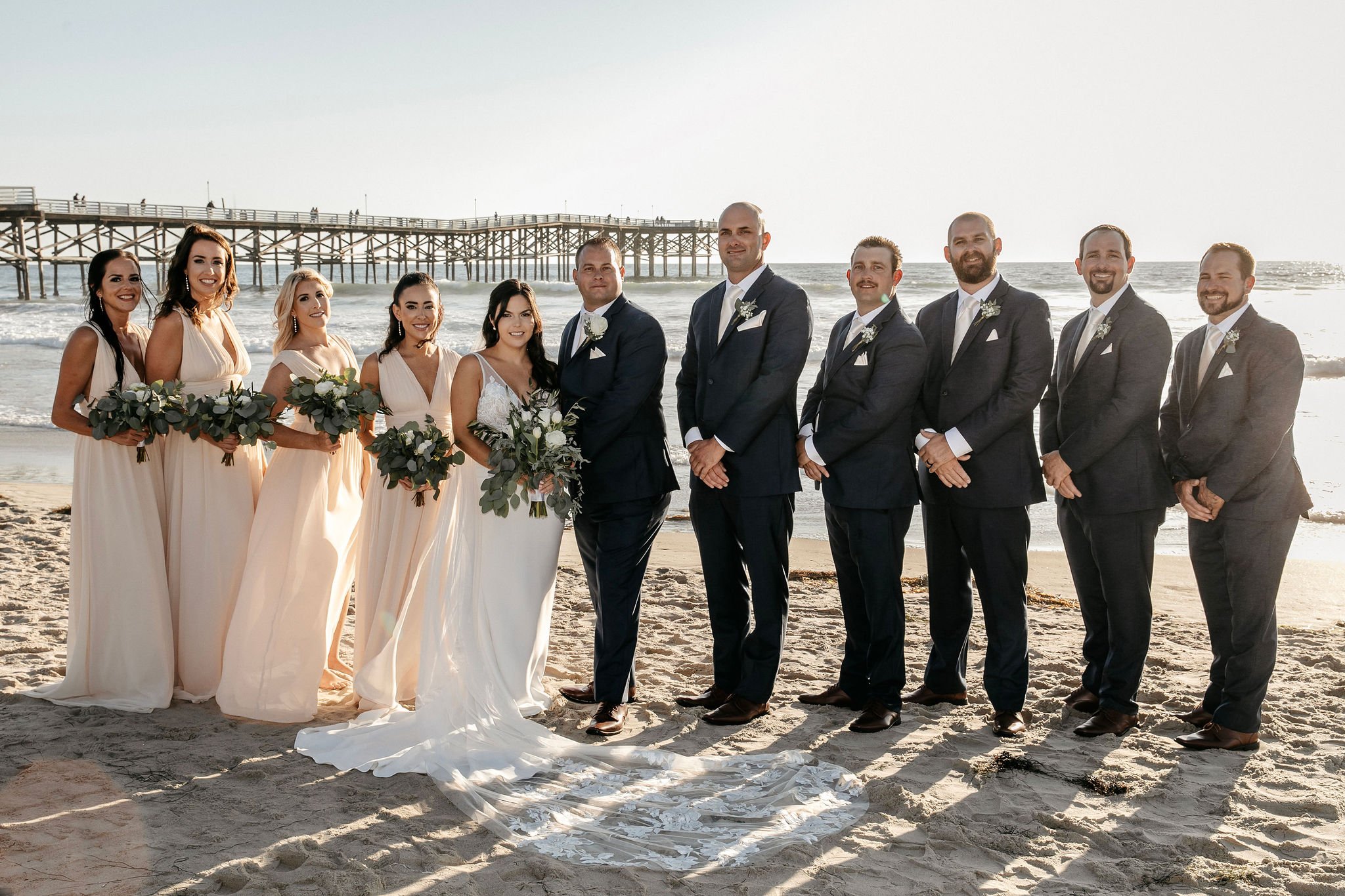 Wedding party gathered on the beach with the bride and groom at sunset, showcasing the work of the best wedding photographers in San Francisco and their ability to capture timeless group portraits.