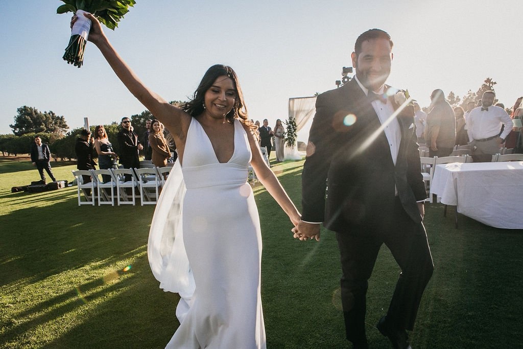 Newlyweds celebrating their ceremony exit with guests in the background, demonstrating how to find a wedding photographer who captures genuine emotions and candid moments.