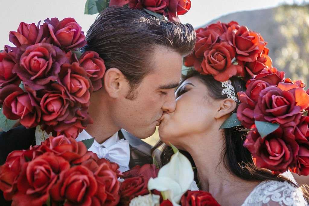 Bride and groom sharing a romantic portrait surrounded by vibrant red florals, showing how to select a wedding photographer whose style matches your vision.