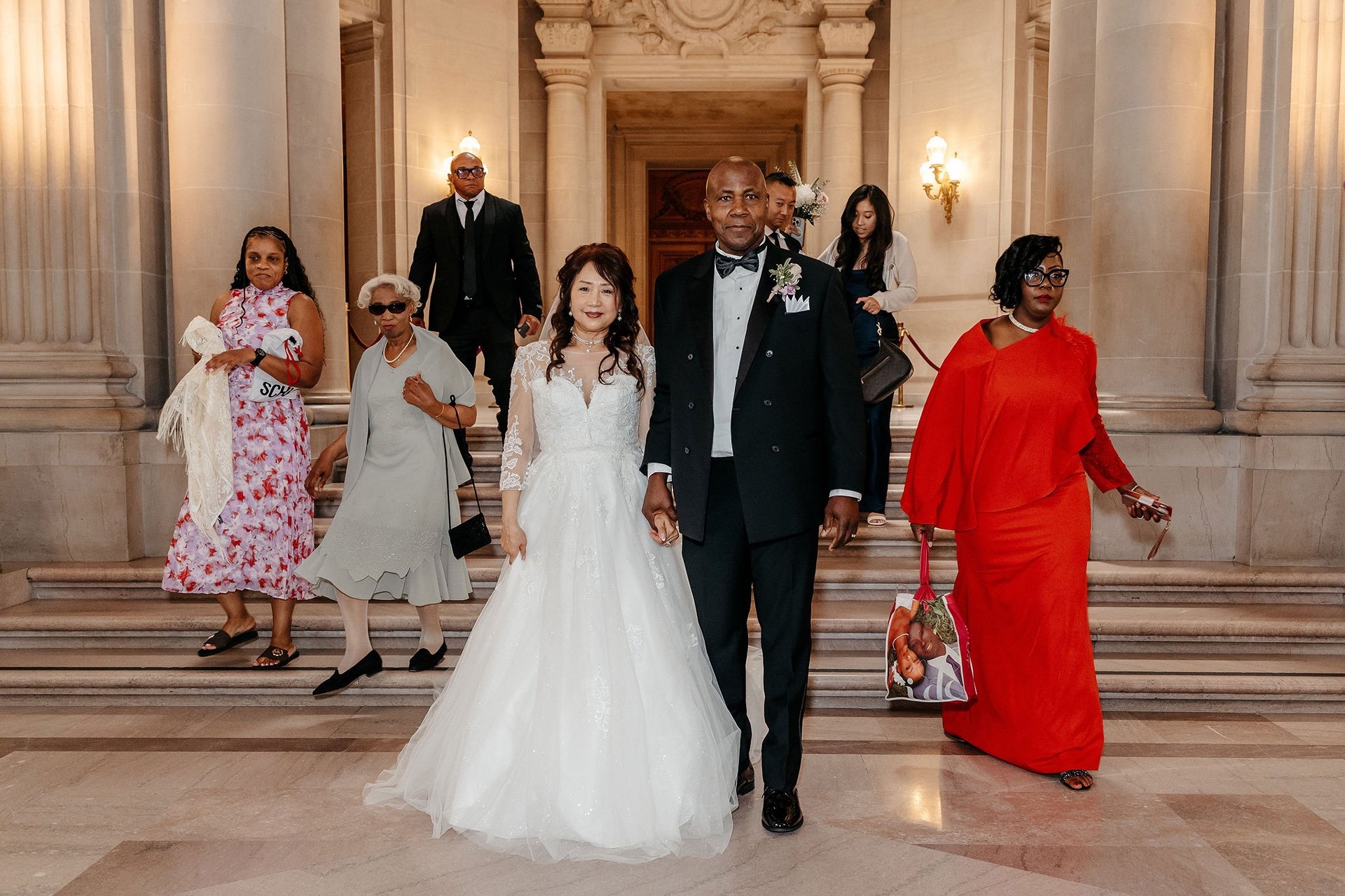 The newly married couple walk down the grand staircase at San Francisco City Hall with their family behind them