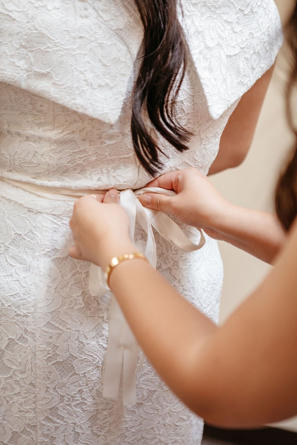 A bridesmaid ties a white bow on the back of a bride